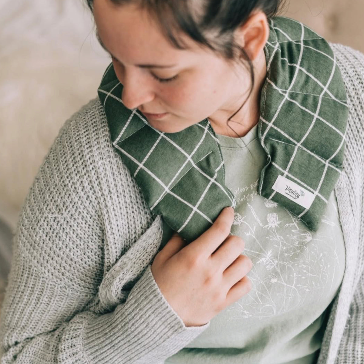 Person holding a green checkered pillow with a visible brand label.