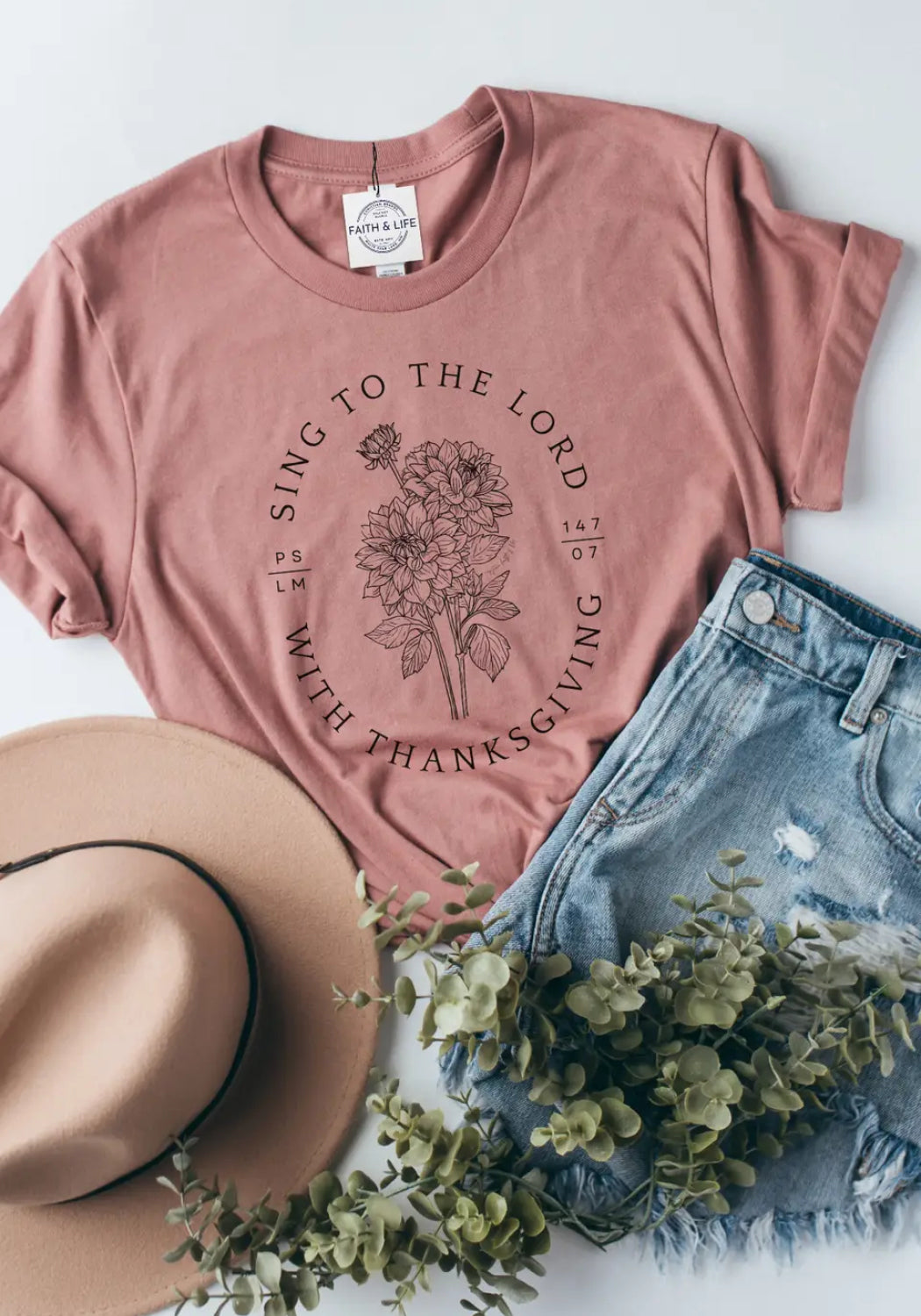 Pink t-shirt with floral design and text, paired with denim shorts and a hat on a light background